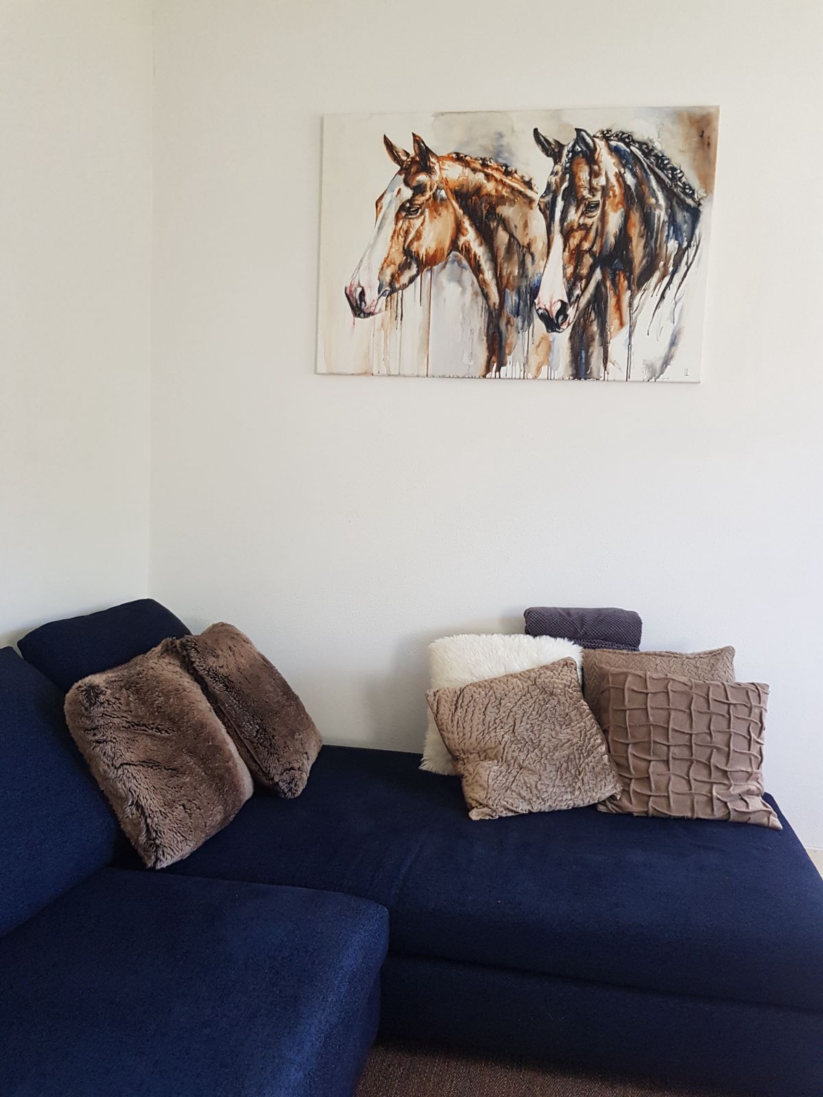 Two horses watercolour above a navy sofa
