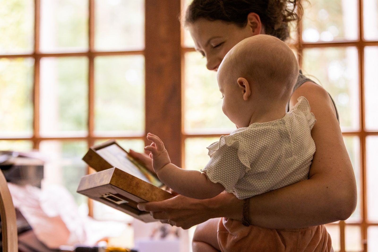 Marjo Lebbe holding a baby reaching towards a framed artwork in warm light