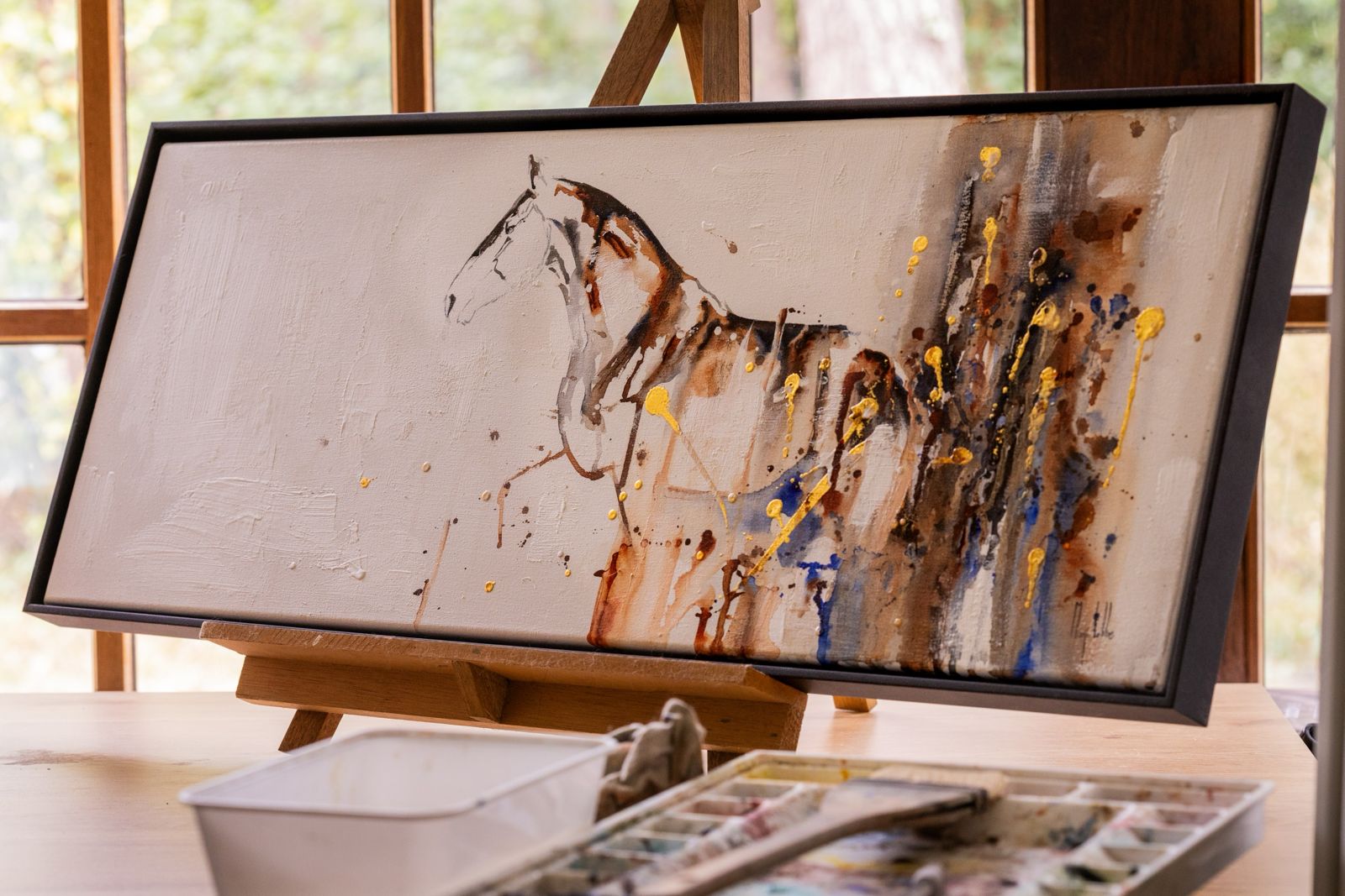 Panoramic framed horse watercolour with gold and blue accents on an easel