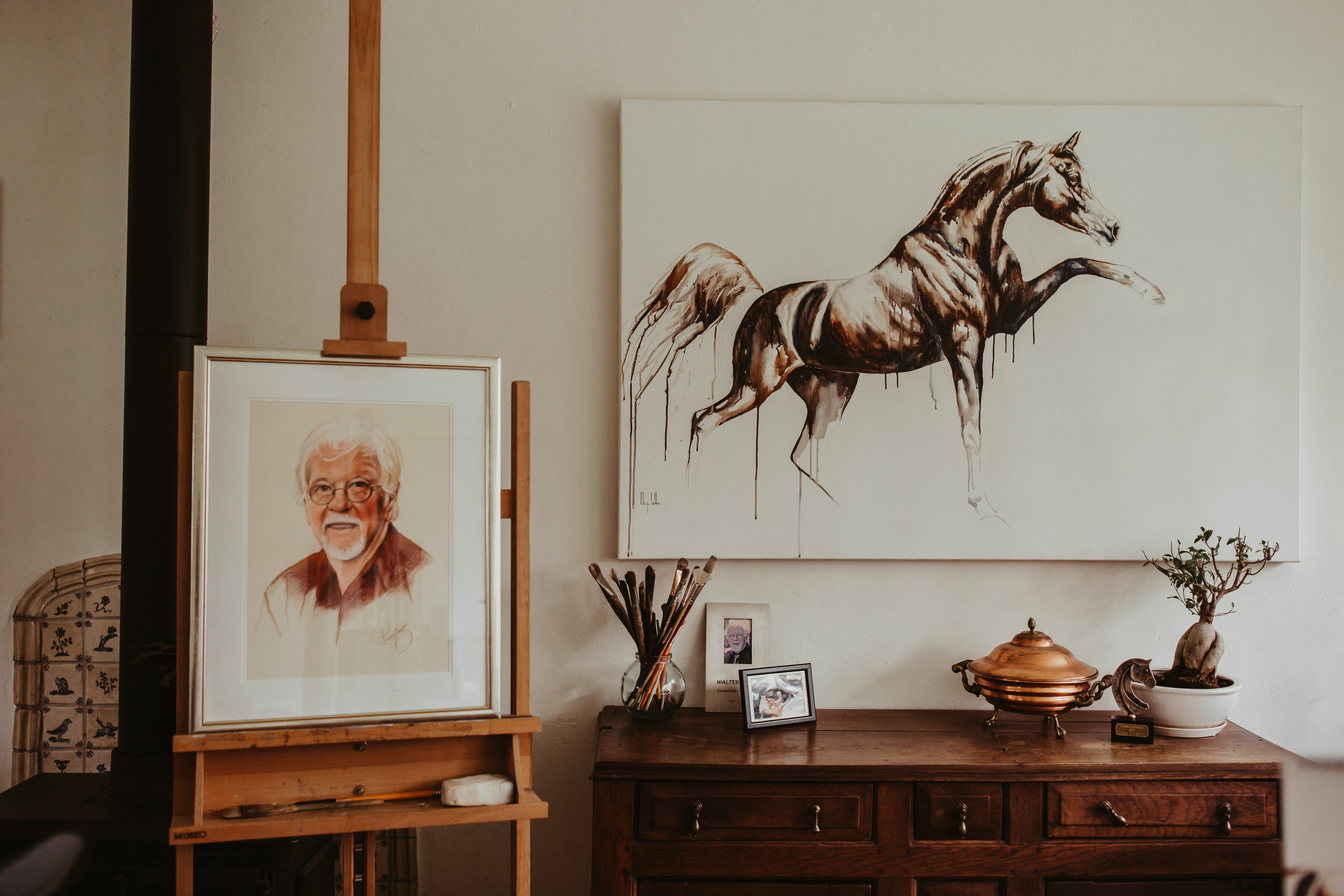 A framed portrait of Marjo's grandfather on the easel in her studio, beside a horse painting