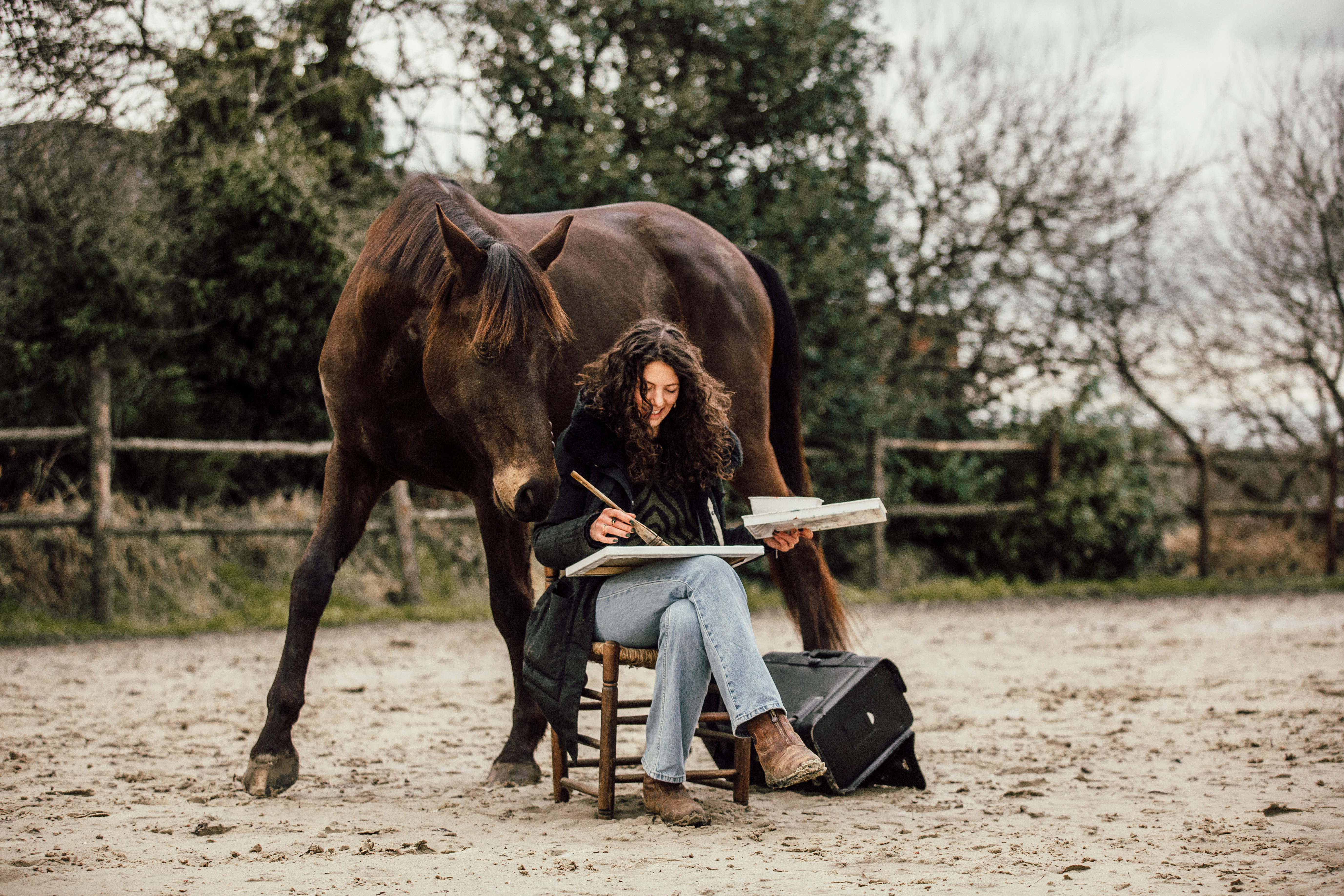 Marjo painting outdoors beside a dark horse in a paddock