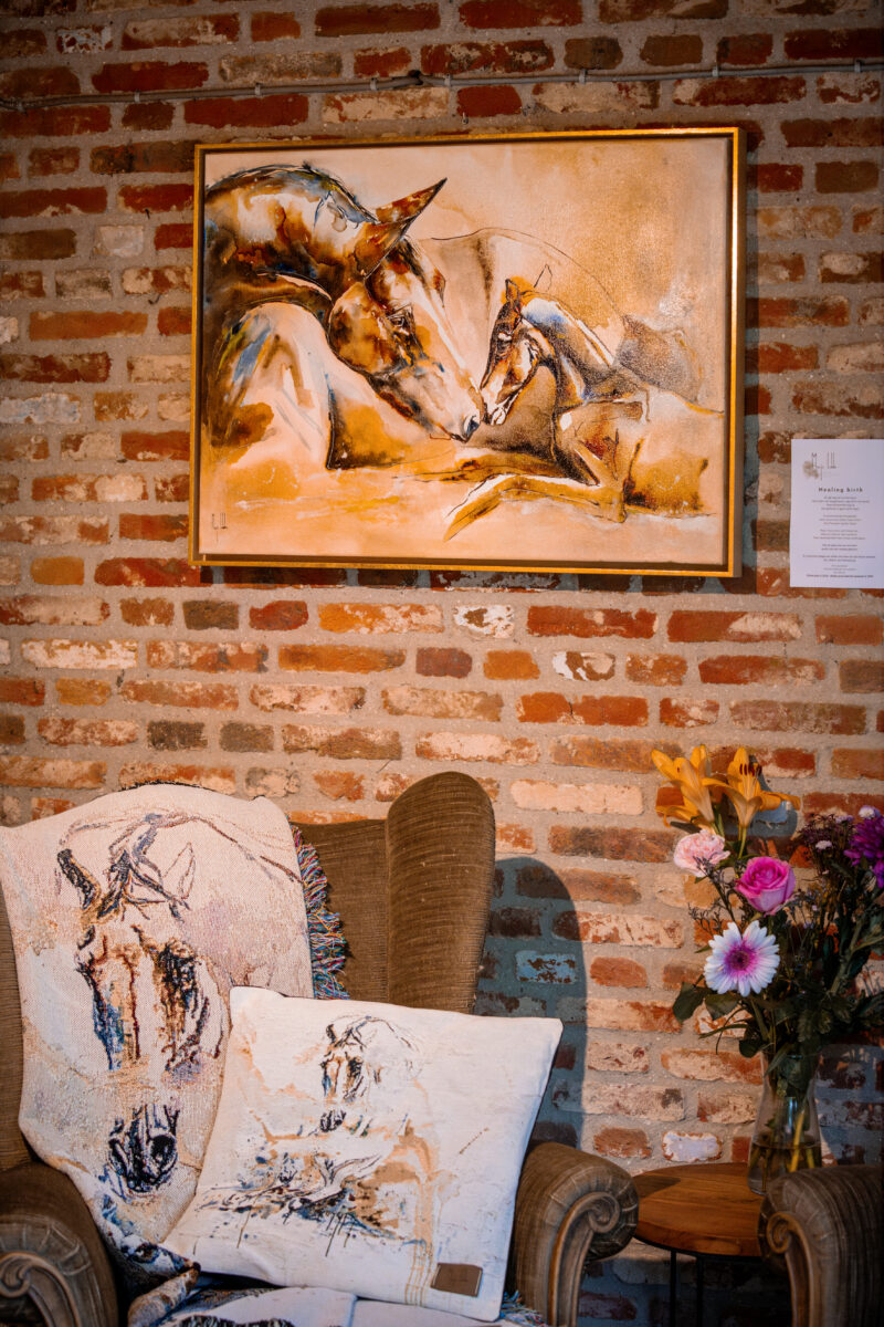 Healing Birth hanging on a rustic brick wall above a cosy armchair with equine cushions