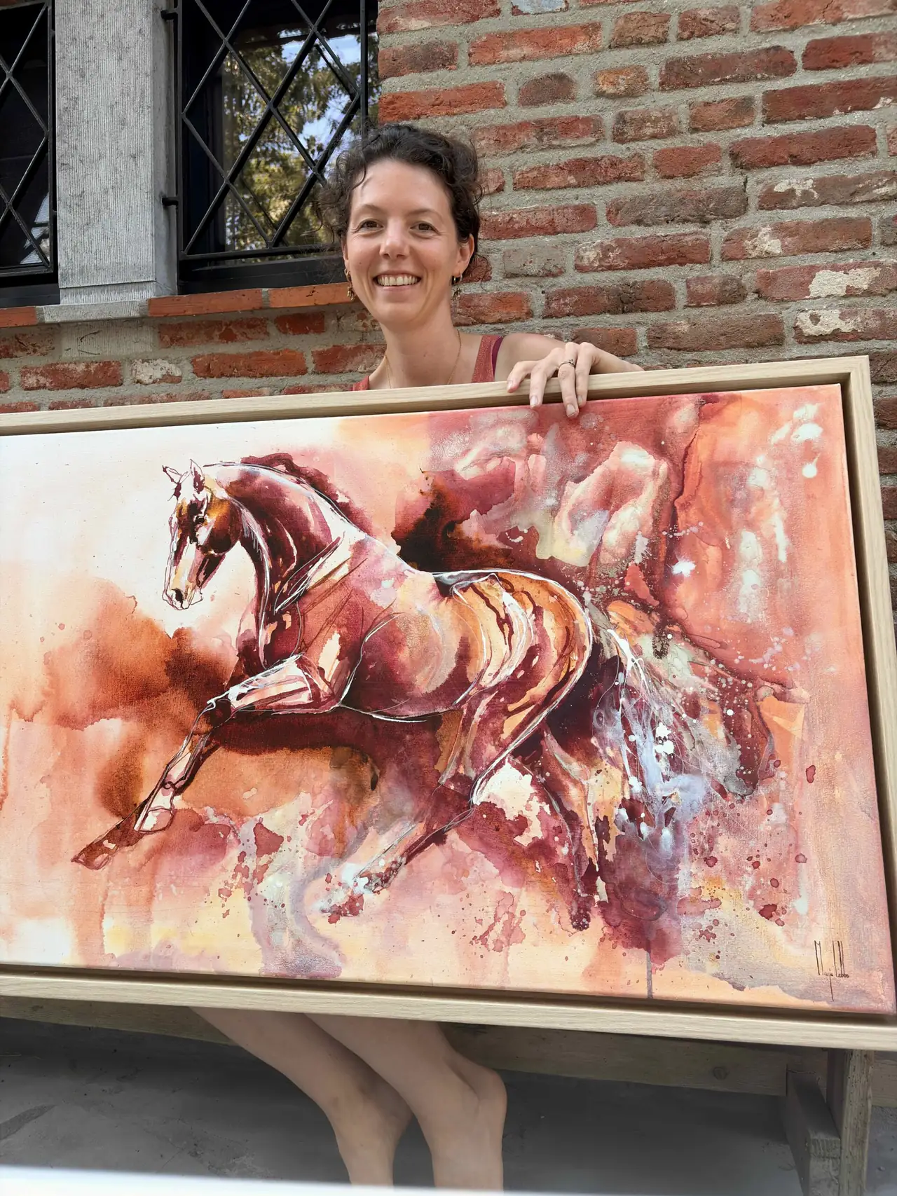 Marjo Lebbe met het ingelijste schilderij Athena voor een bakstenen muur