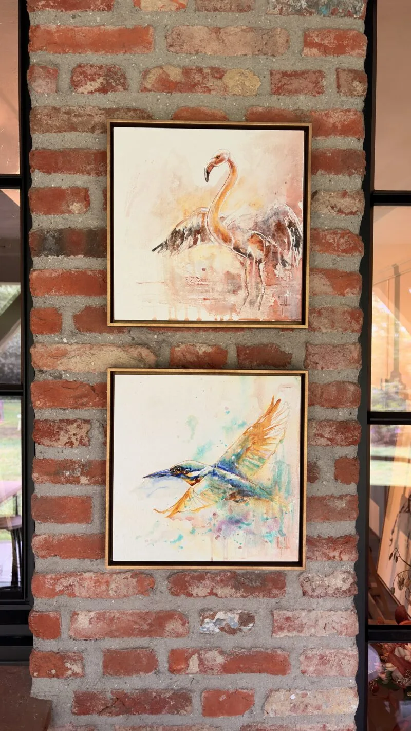 Both Bird Soul panels hung one above the other on a rustic brick wall, the flamingo above the kingfisher in matching gold floating frames