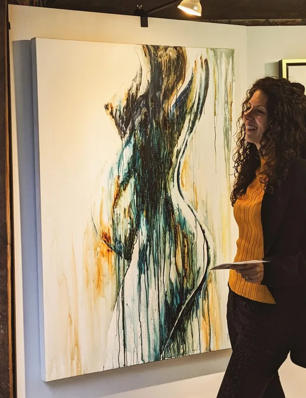 Marjo Lebbe standing beside Elderflower at an exhibition, the canvas hanging on a white wall under gallery lighting
