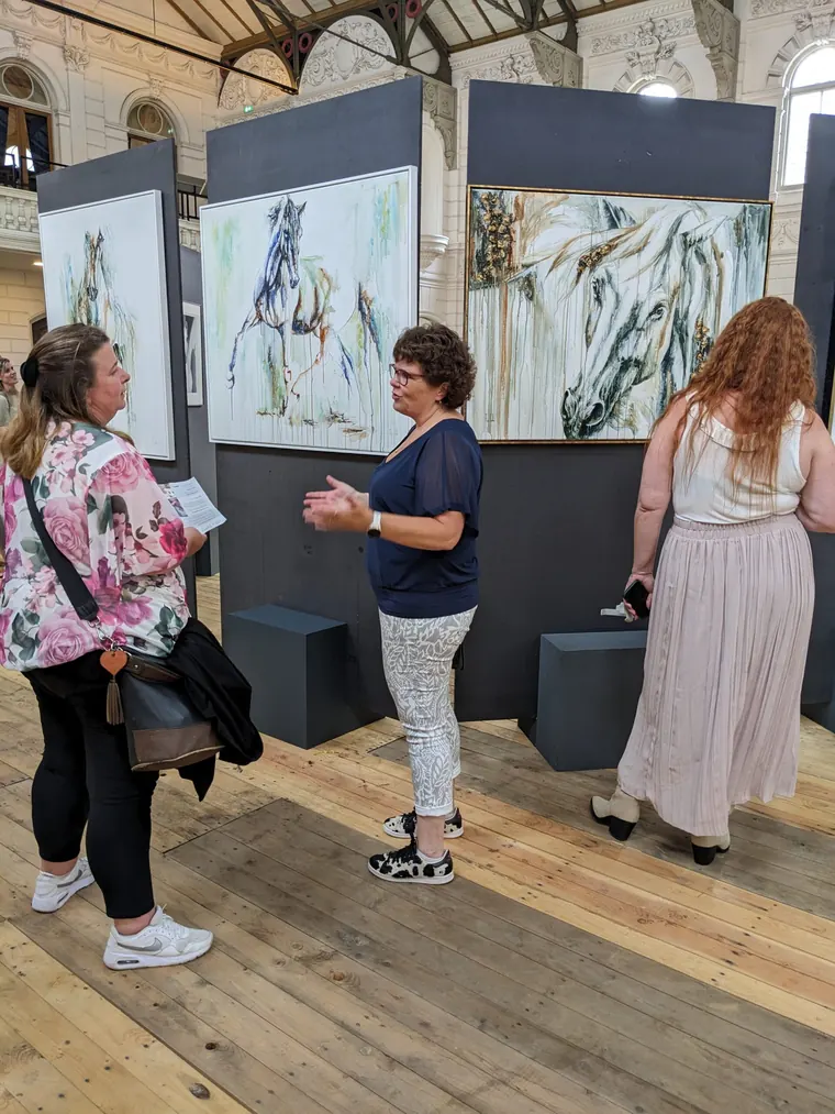Elusive on the middle panel of an exhibition of Marjo Lebbe's horse paintings, visitors talking in front of it