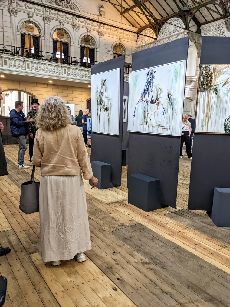The exhibition hall seen wide, Elusive hanging centre on dark panels above a wooden floor