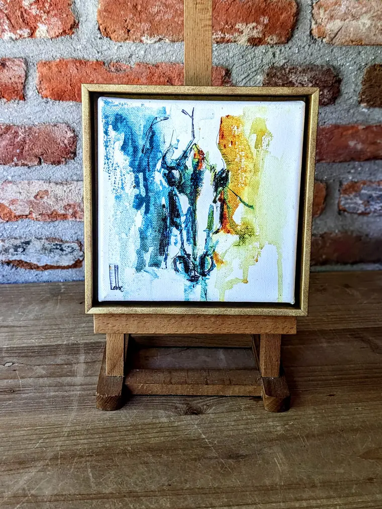 Het blauw- en okerkleurige Small things aquarel op een klein schildersezeltje tegen een bakstenen muur